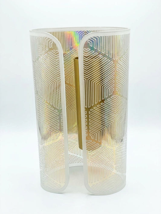 A modern sculptural cylindrical vase or candle holder made of frosted translucent material with an etched geometric circuit pattern, showing a warm gold interior and subtle iridescent rainbow reflections on a white background.