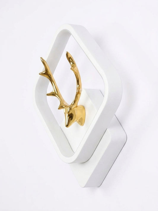A modern white geometric wall sconce featuring a polished gold deer head mounted inside the frame, shown against a plain white background.