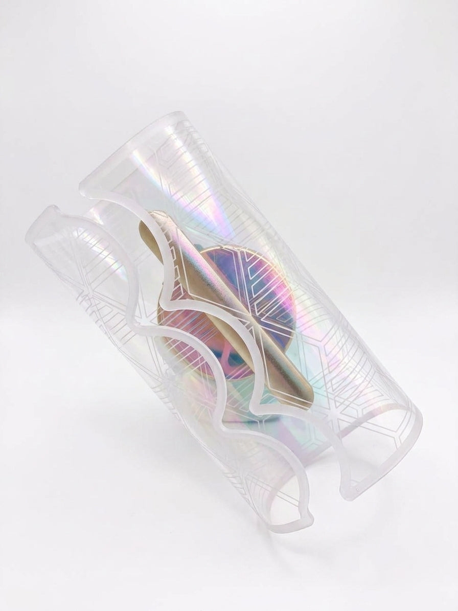 A clear, iridescent plastic sleeve with geometric line patterns, shown containing a gold-colored cylindrical item inside, set against a plain white background.