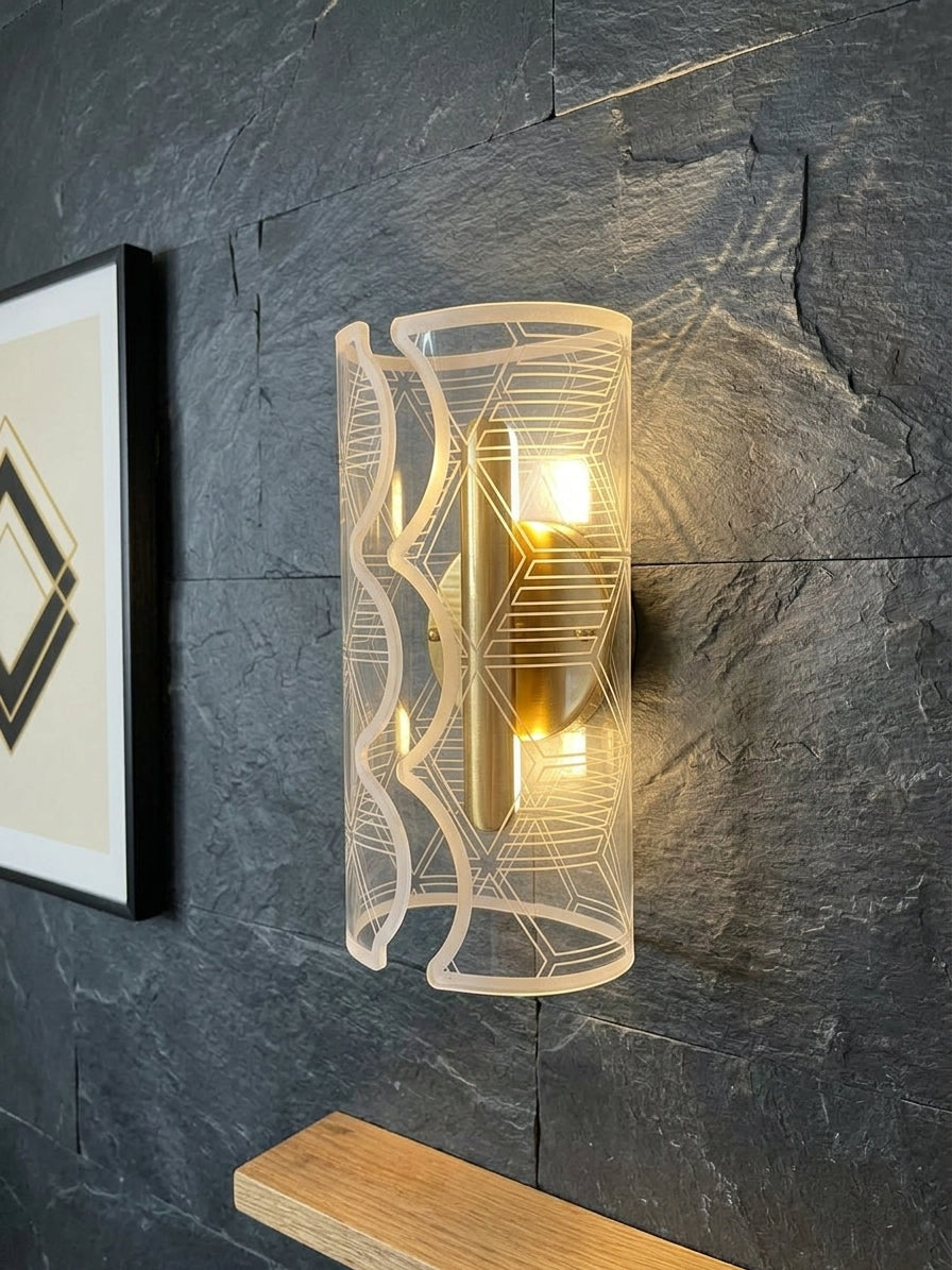 A modern cylindrical wall sconce with a frosted white geometric wireframe cage and a warm glowing light inside, mounted on a dark slate-textured wall next to a framed picture.