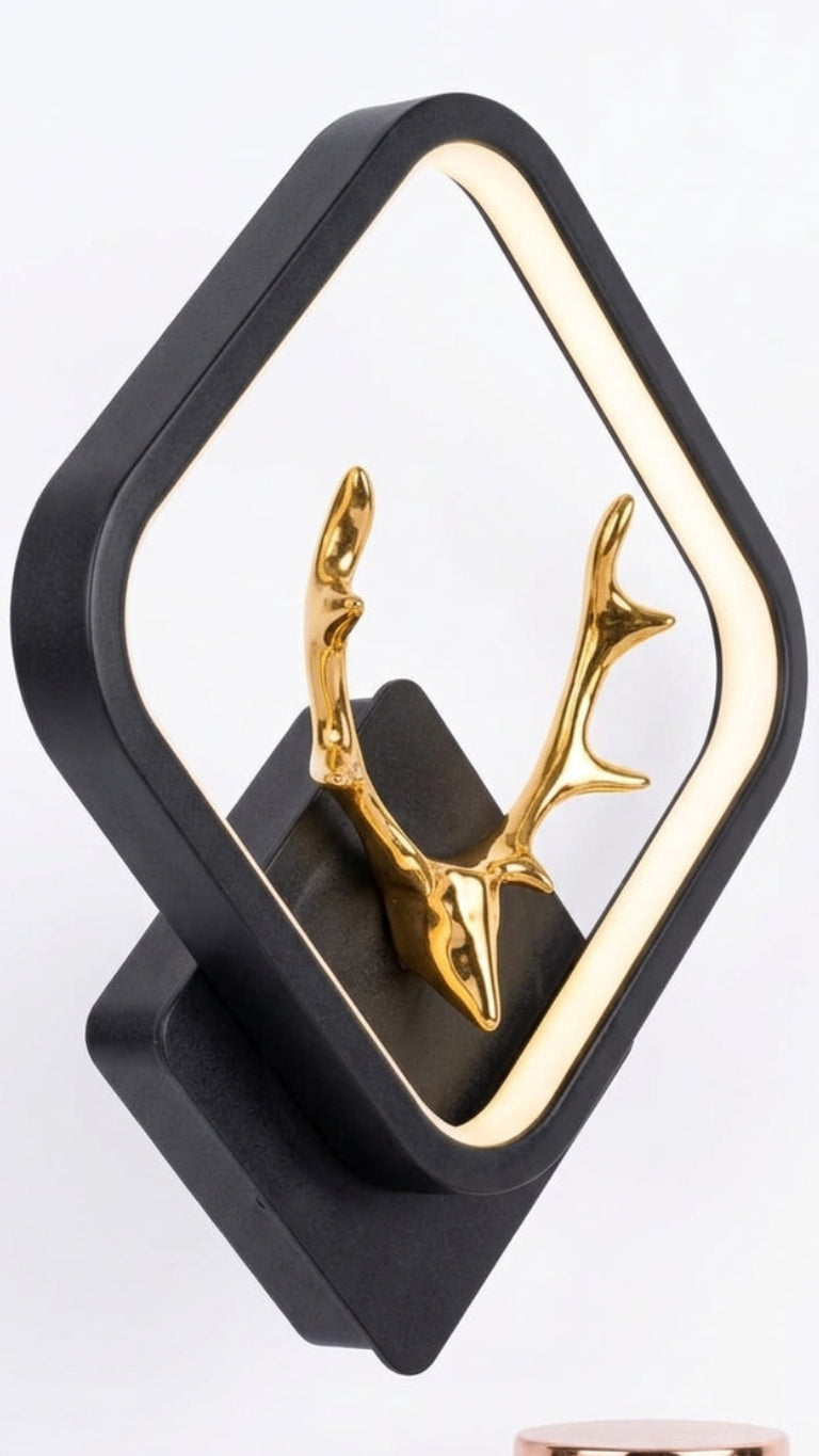 A modern black diamond-shaped wall mirror with a gold deer head antler accent inside, shown on a white background .