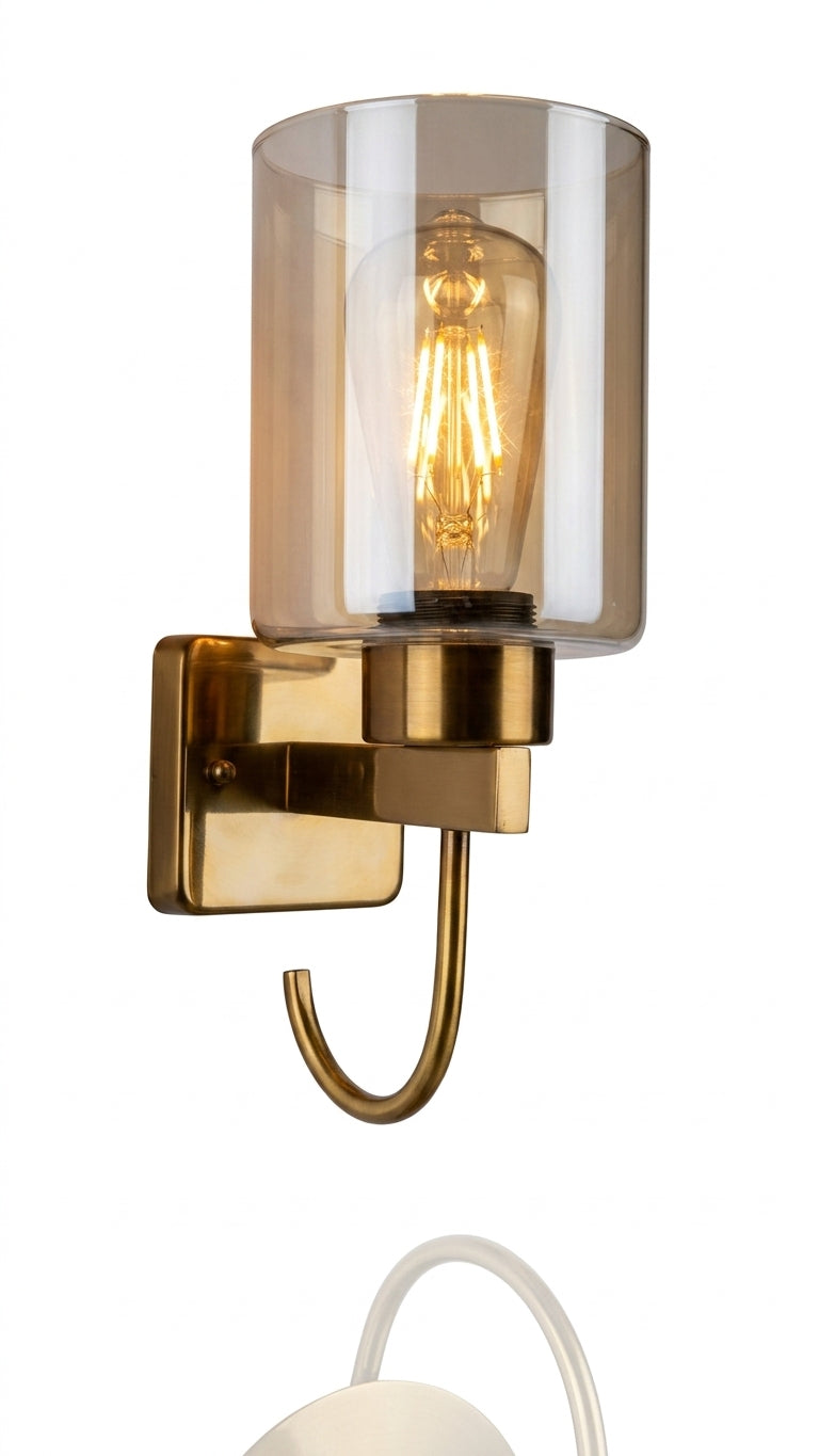A close-up view focusing exclusively on the specific brushed brass wall sconce and the texture of the plaster wall it is mounted on. The glowing vintage filament-style LED bulb is prominent, as is the unique decorative hook at the bottom of the fixture. This view highlights the material contrast between the metal and the fluted glass shade.