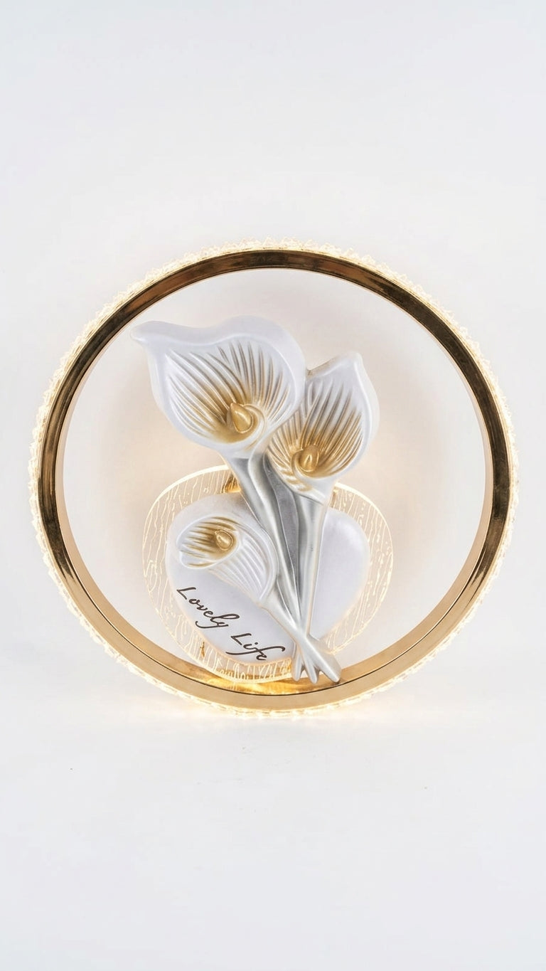 A circular wall art piece featuring three white calla lilies with gold accents and a gold outer ring, mounted on a white wall.