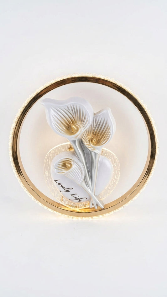 A circular wall art piece featuring three white calla lilies with gold accents and a gold outer ring, mounted on a white wall.