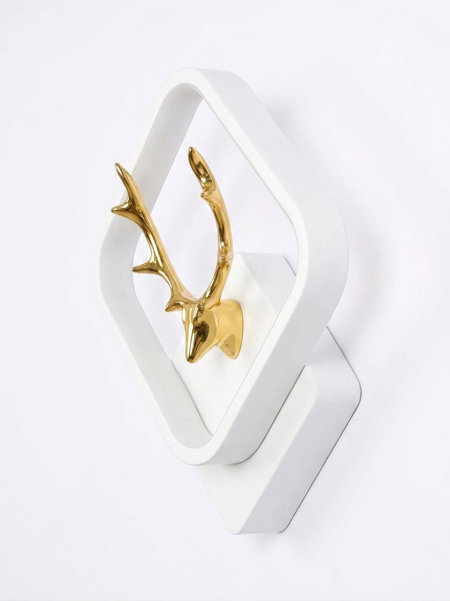 A modern white geometric wall sconce featuring a polished gold deer head mounted inside the frame, shown against a plain white background.